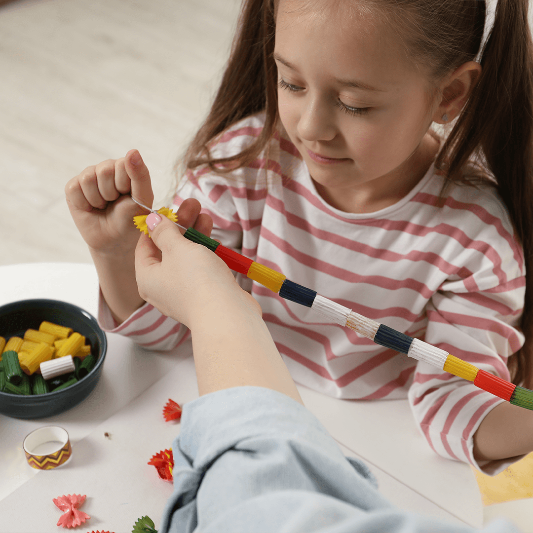 Tyttö ja äiti tekevät makaronikorua – luovaa tekemistä lapsille kotona.