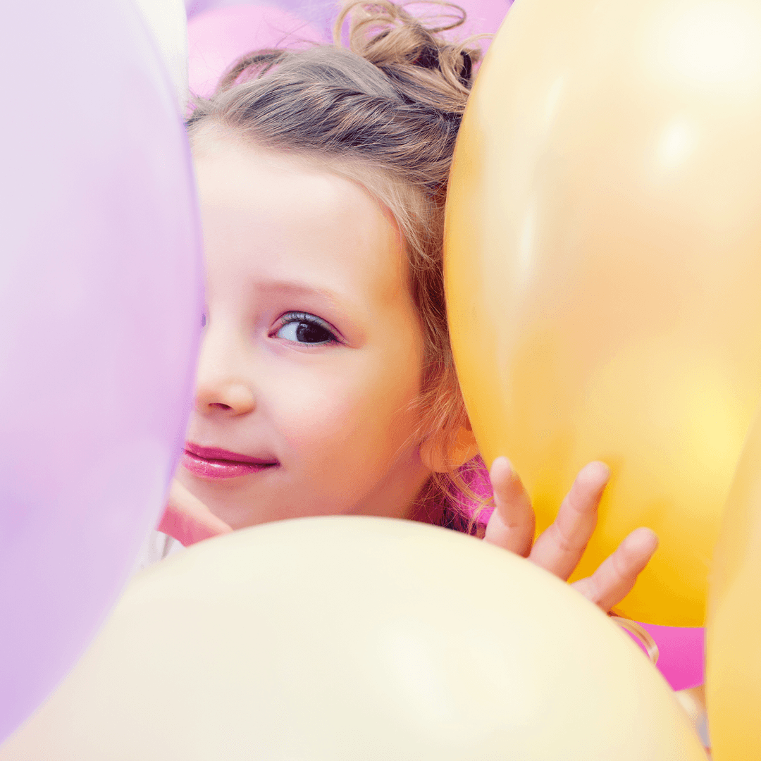 Tyttö kurkistaa ilmapallojen takaa – lasten synttäri ideat täynnä iloa