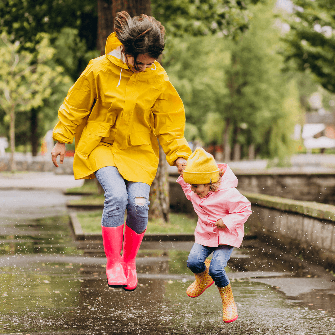 Mom and daughter jumping in puddles – outdoor fun for a rainy day with kids.