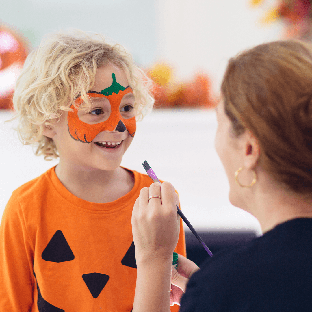 Äiti maalaa pojalle kurpitsakuvion kasvoihin halloweenissa